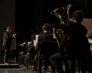 Waving his baton to the rhythm of the music, band teacher Evan Rogovin leads the Symphonic Band and Wind Ensemble musicians as they focus on their parts during the Fall Band Concert. On Oct. 1, the music department held its first band performance of the year in Meyer Hall. “After not getting to play in front of people all summer, it was refreshing to be back on a stage with an audience and with my band family,” band sophomore Luna Schneider said. 
