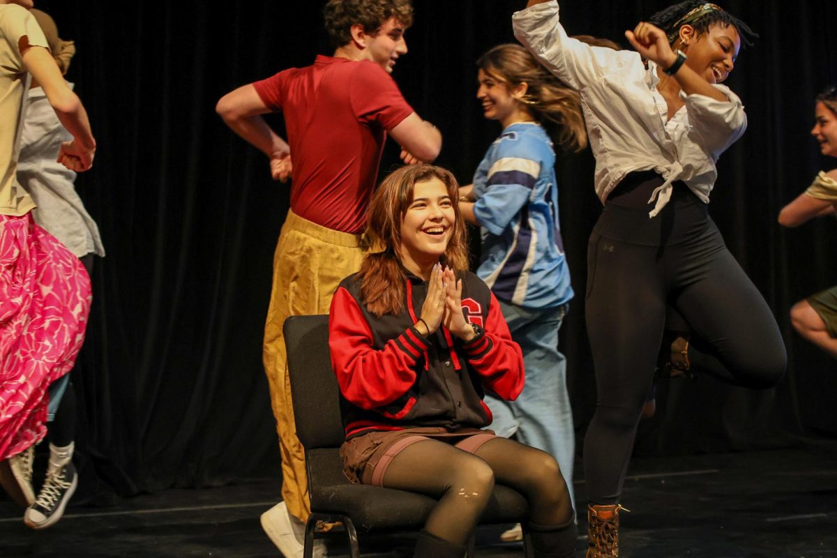 Applauding the other actors dancing around her, Oliver sits in the middle of the Black Box Theater during the musical piece “Gaston” from the musical “Beauty and the Beast.” 