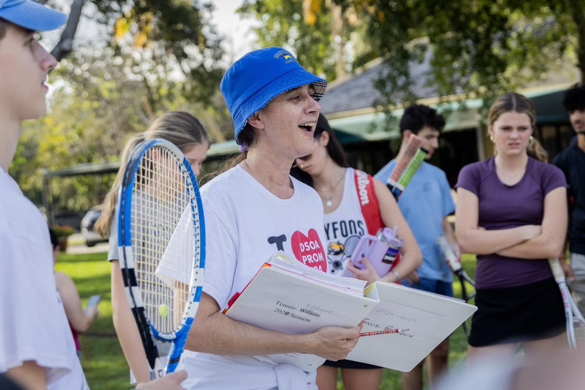 Surrounded by players, tennis coach and Spanish teacher Marina Ratchford talks about pre-practice plans, upcoming games, and match-ups between students in determining game-day lineups for both the boys and girls teams.